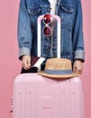 Young woman traveler holding pink suitcase and passport document over pink background