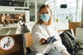 Young woman traveler in medical mask sits in the waiting room and holds out passport and ticket.. Royalty Free Stock Photo