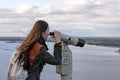 A young woman traveler on the observation deck looking through binoculars at the panorama of the city of Nizhny Novgorod Royalty Free Stock Photo