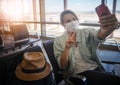 Young woman traveler in a protective medical mask with a backpack sits in the waiting room and doing selfie, video chatting on