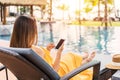 Young woman traveler relaxing and using a mobile phone by a hotel pool while traveling for summer Royalty Free Stock Photo
