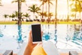 Young woman traveler relaxing and using a mobile phone by a hotel pool while traveling for summer vacation Royalty Free Stock Photo