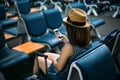 Young woman traveler sitting while using smartphone on chair of passenger in an airport lounge waiting for flight aircraft at Royalty Free Stock Photo