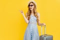 Young woman traveler with suitcase, in summer hat points to copy space on isolated yellow background Royalty Free Stock Photo