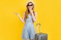 Young woman traveler with suitcase, in summer hat points to copy space on isolated yellow background Royalty Free Stock Photo