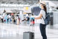 Young woman traveler wearing face mask and nitrile glove holding handle luggage in airport terminal, protection Coronavirus