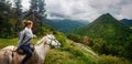 Young woman travels during summer vacation riding horse high in mountains and watches herd of sheep graze against Royalty Free Stock Photo