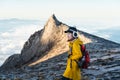 Young woman trekker with backpack standing in front of South peak of Kinabalu mountain massif, Borneo island in Sabah state,
