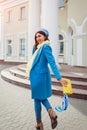 Young woman in trendy blue coat walking in city holding stylish handbag. Spring female clothes and accessories. Fashion