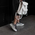 Young woman in a trendy dress with a stylish white leather backpack in silver leather fashionable modern sneakers stands in a room Royalty Free Stock Photo