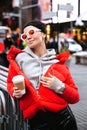 Young woman in trendy eyeglasses drink coffee on Time Square. Model in street style outfit, NY city Royalty Free Stock Photo