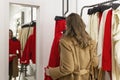 A young woman tries on a dress in front of a mirror in a clothing store. Beautiful smiling blonde in a beige coat