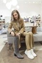 Young woman trying on boots in a shoe store. Beautiful smiling blonde is sitting on the couch. Fashion, style and beauty. Vertical Royalty Free Stock Photo