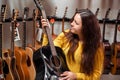 Young woman trying and buying a new wooden guitar in instrumental or musical shop, instrument concept