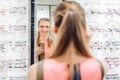 Young woman trying fashionable glasses in optometrist store