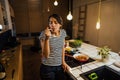 Young woman trying out healthy meal in home kitchen.Making dinner on kitchen island standing by induction hob.Preparing fresh Royalty Free Stock Photo