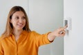 Young woman turns down the temperature for energy saving. Girl adjusting digital central heating thermostat at home. Focus on the Royalty Free Stock Photo