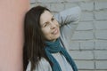 A young woman in a turquoise scarf and a gray sweater with loose dark hair stands against the wall and looks away into the Royalty Free Stock Photo