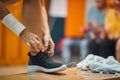 Young woman tying her shoe in gym locker room, with earphones and towel on bench, getting ready for workout