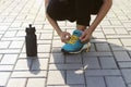 Young woman tying shoelaces on sneakers on a pavers. Standing next to a bottle of water. Exercise outdoors Royalty Free Stock Photo