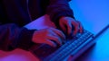 A young woman is typing on a laptop keyboard. Hands close up. Hacker makes a hack through a laptop. Blue and red light