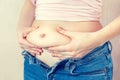 A young woman in unbuttoned trousers holds her hands, squeezes belly fat at the waistline, cannot fasten a button on jeans. The Royalty Free Stock Photo