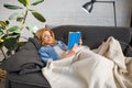 Young woman under a blanket reading book on couch Royalty Free Stock Photo