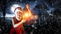Young woman in a uniform of Santa Claus with a lit lantern on a winter Christmas night background. Royalty Free Stock Photo