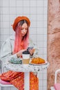 Young woman with unique style having breakfast in cafe and using mobile phone.