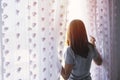 Young woman unveil curtain and looking out of window in the morning