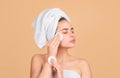 Young woman use micellar water and circle white pad, enjoys spa procedures, wrapped towel on head, isolated on beige Royalty Free Stock Photo