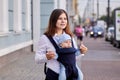 Young woman uses baby carrier or sling while walking outside with her four month old son. Royalty Free Stock Photo