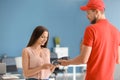 Young woman using bank terminal to pay for food delivery indoors