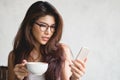 Young woman using cellphone texting and drinking coffee in cup. Royalty Free Stock Photo