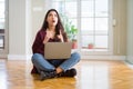 Young woman using computer laptop sitting on the floor amazed and surprised looking up and pointing with fingers and raised arms Royalty Free Stock Photo