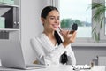 Young woman using cosmetic pocket mirror while applying makeup in office Royalty Free Stock Photo