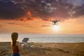 Young woman using drone at sunset for photos and video making - Happy woman having fun with new technology trends in sky and sea. Royalty Free Stock Photo