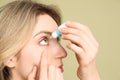 Young woman using eye drops on pale olive background, closeup Royalty Free Stock Photo