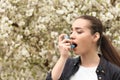 Young woman using inhaler near blooming tree. Allergy concept Royalty Free Stock Photo