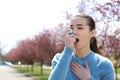 Young woman using inhaler near blooming trees. Allergy concept Royalty Free Stock Photo