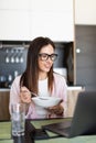 Young cheerful woman using on laptop computer and eating breakfast in the kitchen Royalty Free Stock Photo