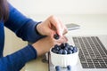 Young woman using laptop computer at home and eating blueberry.