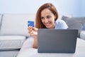 Young woman using laptop and credit card lying on sofa at home Royalty Free Stock Photo