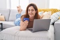 Young woman using laptop and credit card lying on sofa at home Royalty Free Stock Photo