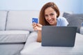 Young woman using laptop and credit card lying on sofa at home Royalty Free Stock Photo