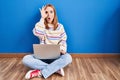 Young woman using laptop at home sitting on the floor doing ok gesture shocked with surprised face, eye looking through fingers Royalty Free Stock Photo