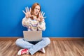Young woman using laptop at home sitting on the floor doing stop gesture with hands palms, angry and frustration expression Royalty Free Stock Photo