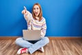 Young woman using laptop at home sitting on the floor pointing with finger surprised ahead, open mouth amazed expression, Royalty Free Stock Photo