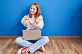 Young woman using laptop at home sitting on the floor pointing to you and the camera with fingers, smiling positive and cheerful Royalty Free Stock Photo