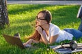 Young woman using laptop in the park lying on the green grass. Leisure time activity concept. Royalty Free Stock Photo